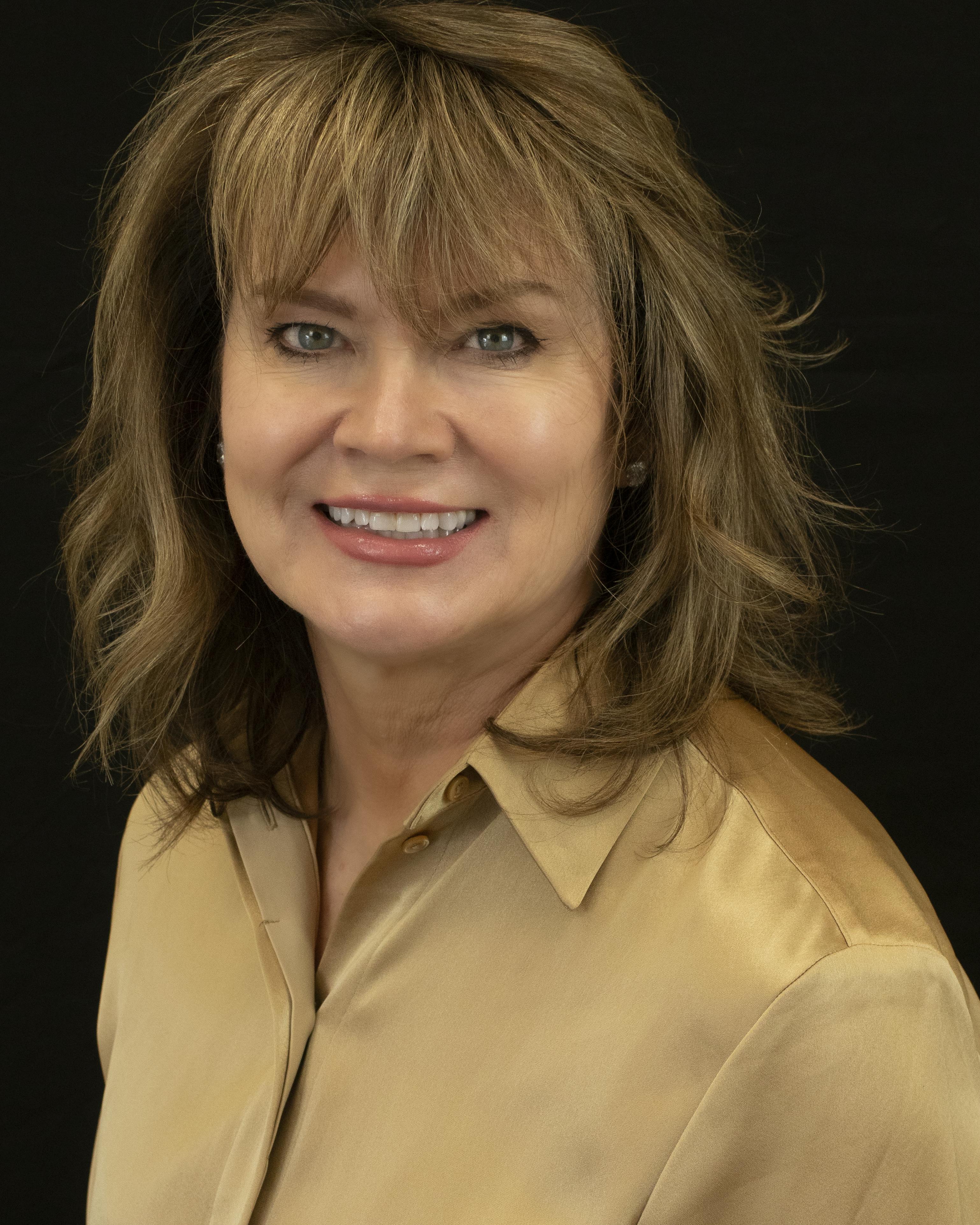 Cindy Greenfield, PT, wearing a tan jacket over a white shirt in front of a blue background